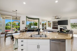 A modern kitchen with a central island, built-in appliances, and a dining area with a view of the outdoors. - Stunning Private Pool Home Overlooking the 8th and 9th Double Fairway in PGA (La Quinta)