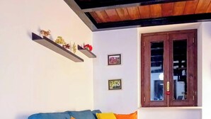 Uma sala de estar com um sofá azul, almofadas amarelas e laranja, um radiador, piso de madeira, um aquecedor branco e um armário de madeira com portas de vidro.