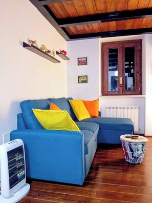 Ein Wohnzimmer mit einem blauen Sofa, gelben und orangen Kissen, einem Heizkörper, Holzboden, einer weißen Heizung und einem Holzschrank mit Glastüren.