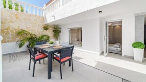 Een modern terras buiten met een eettafel en stoelen, een stenen muur en uitzicht op het interieur.
