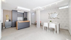 Een moderne keuken met een centraal eiland, een eethoek met witte stoelen, en behang met een patroon op de muren.