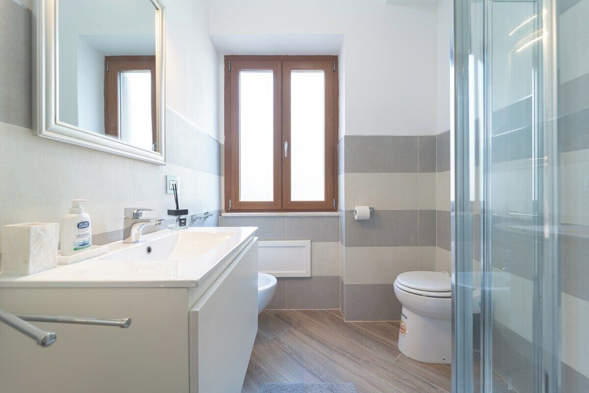 A modern bathroom with a large mirror, a sink, a toilet, and a shower area.