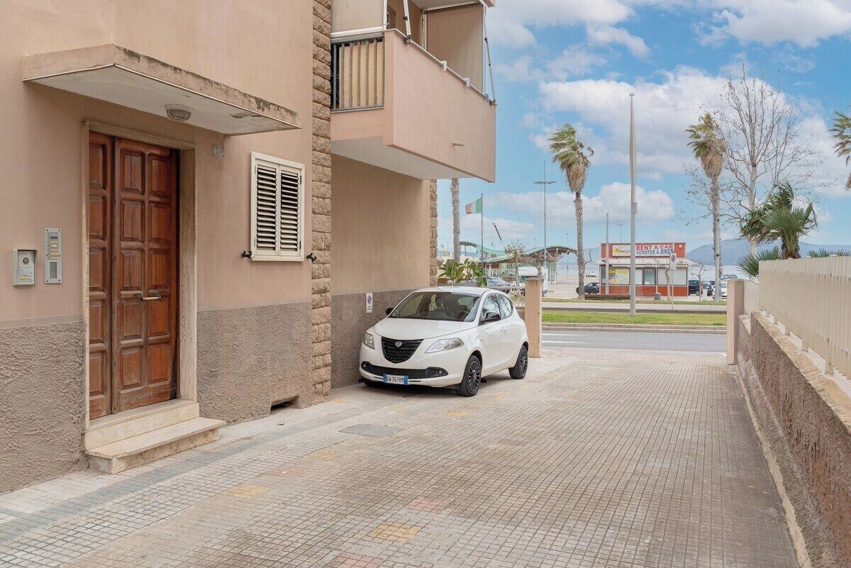 Un coche blanco aparcado frente a un edificio con puerta de madera y ventana con contraventanas.