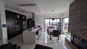 A modern kitchen with a central island, a dining area with a view, and a living space with a fireplace. - Villa with sea and mountain views (FURIANI)