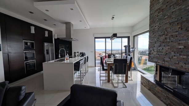 A modern kitchen with dark cabinetry, a central island, and a dining area with a view. - Villa with sea and mountain views (FURIANI)