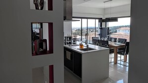 A modern kitchen with a central island, large windows offering a city view, and a dining area with a table set for two. - Villa with sea and mountain views (FURIANI)