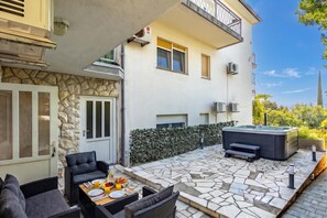 Eine Terrasse mit Gartenmöbeln, einem Whirlpool und einem Boden aus Steinplatten.