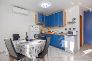 Une cuisine compacte avec des meubles bleus, un réfrigérateur blanc, un four à micro-ondes et un coin repas avec une table dressée pour deux personnes.