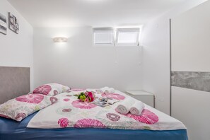 Siististi pedattu sänky, jossa on kukkakuviollinen päiväpeite, kaksi tyynyä, maljakko täynnä kukkia ja rullalle taitetut pyyhkeet.