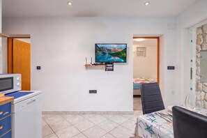 Ein modernes Wohnzimmer mit einem wandmontierten Flachbildfernseher, einem Essbereich mit Tisch und Stühlen und einer Küchenzeile mit Mikrowelle und Kühlschrank.