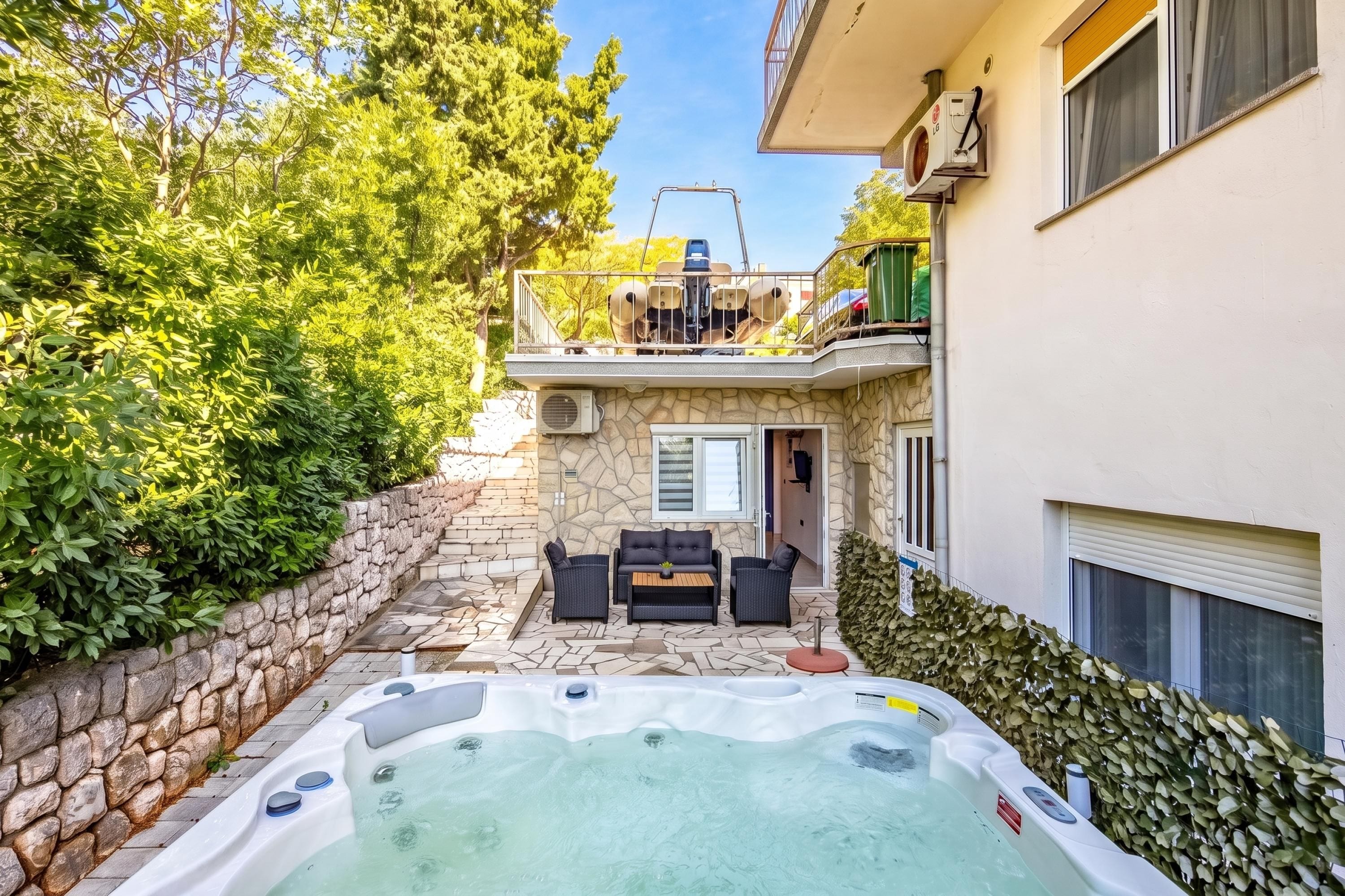 Ein Whirlpool in einem Garten mit Steinmauern, eine Terrasse mit Gartenmöbeln und ein Gebäude mit einem Balkon.