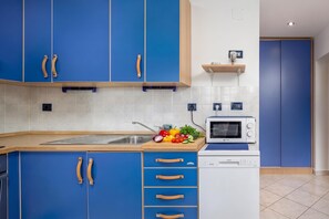 Eine moderne Küche mit blauen Schränken, einer Mikrowelle und einem Schneidebrett mit Gemüse.
