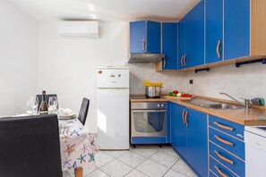 Eine kleine Küche mit blauen Schränken, einem weißen Kühlschrank und einem Essbereich mit Tisch für zwei Personen.