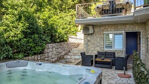 Un jacuzzi en un área exterior con paredes de piedra, mobiliario de mimbre y un balcón.