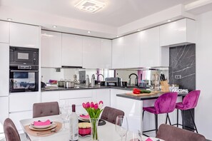 A modern kitchen with white cabinetry, a built-in oven, and a dining area with a table set for two. - Comfortable Seaview Apartment Pacco (Novi Vinodolski)