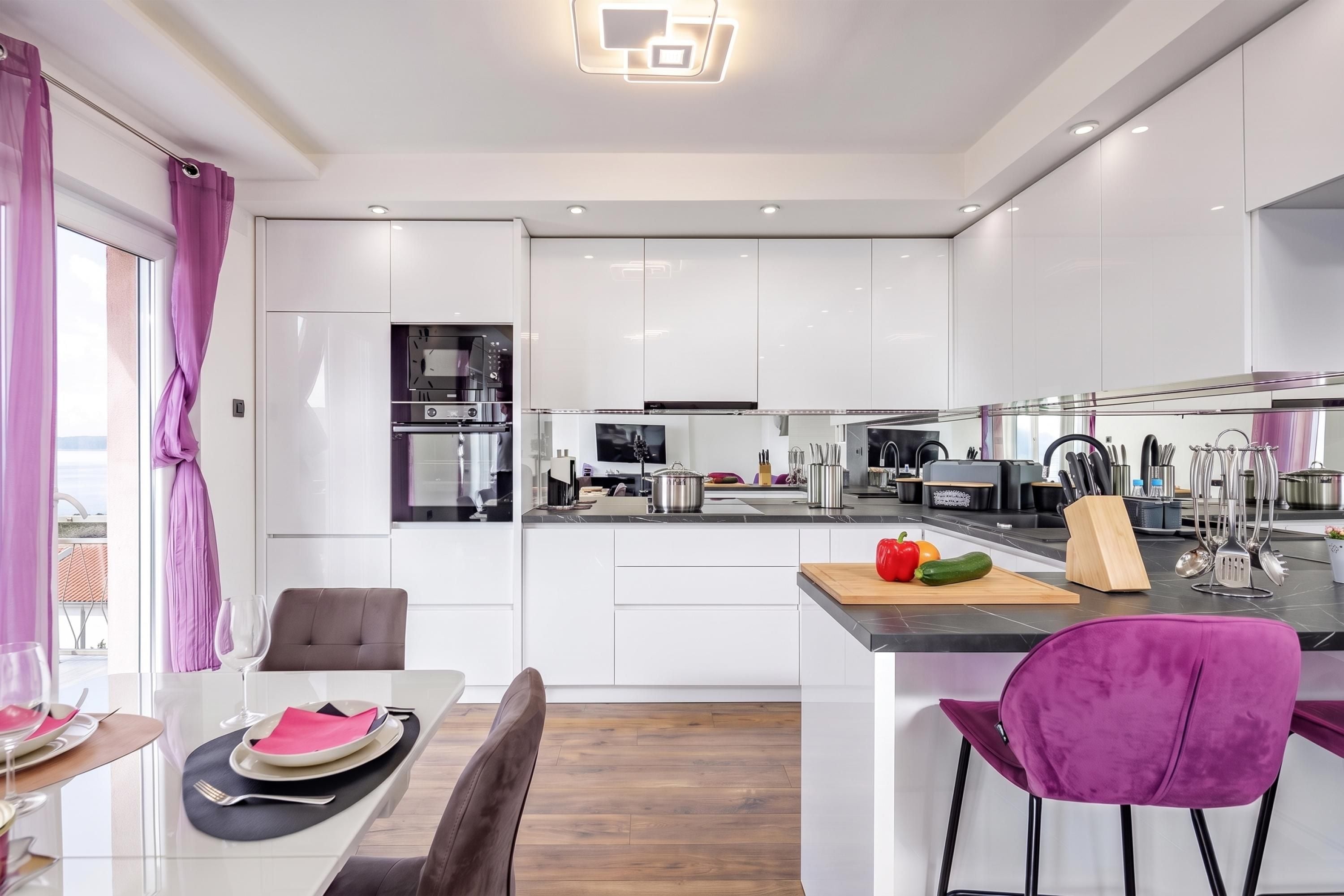 Een moderne keuken met witte kasten, een centraal eiland en een eethoek met een tafel gedekt voor twee personen.