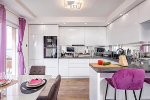 A modern kitchen with white cabinets, a central island, and a dining area with a table set for two. - Comfortable Seaview Apartment Pacco (Novi Vinodolski)