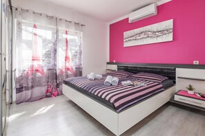 A modern bedroom with a bed, a bedside table, a small potted plant, and a wall-mounted air conditioner. - Comfortable Seaview Apartment Pacco (Novi Vinodolski)