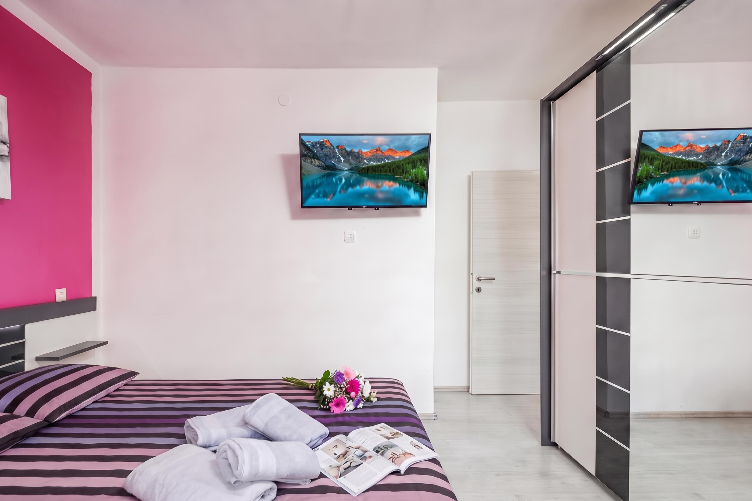 Une chambre moderne avec un lit, un téléviseur à écran plat fixé au mur et un placard à portes coulissantes.