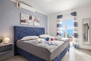 A modern bedroom with a large bed, a bedside table with a lamp, a painting on the wall, and a view through the window. - Comfortable Seaview Apartment Pacco (Novi Vinodolski)