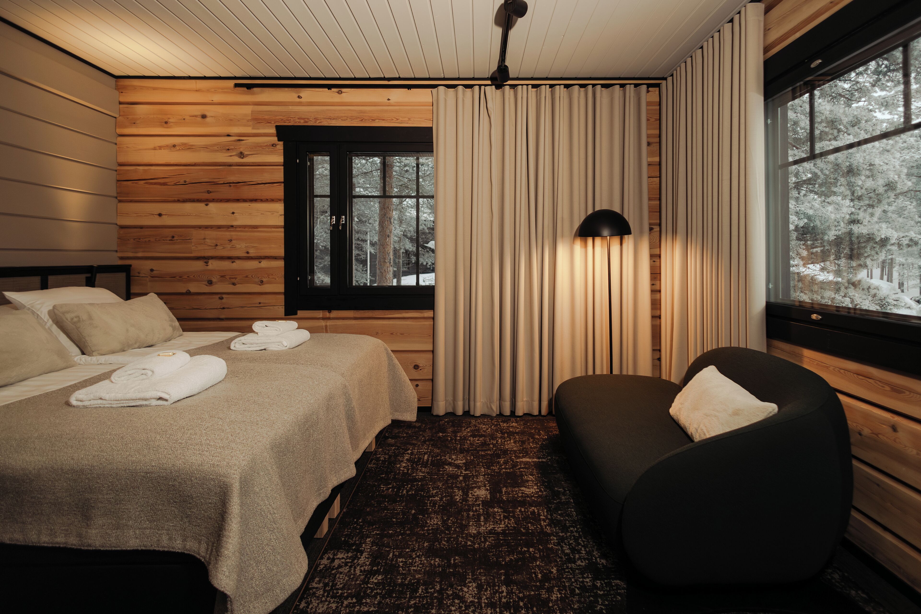 Ett rum inrett som en stuga, med träpanel, en säng, en soffa och ett fönster med gardiner.