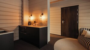 A compact kitchen with a built-in stove, a coffee maker, and a sink. There is a dark wooden door and a striped sofa in the room. - Northern Lights Village Ivalo (Inari)