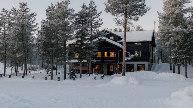 A large, dark wooden lodge surrounded by snow-covered trees. - Northern Lights Village Ivalo (Inari)