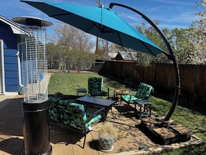 Un patio con mobiliario exterior, una parrilla y un paraguas grande.