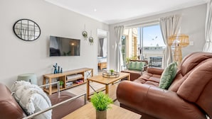 A modern living room with a brown leather sofa, a wooden coffee table, and a TV mounted on the wall. - Coral Grove (Cape Town)