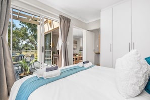 A hotel room with a bed, a view of the outdoor patio, and a dining area visible through an open door. - Coral Grove (Cape Town)