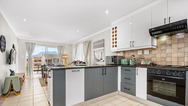 A modern kitchen with grey and white cabinetry, a large island, and a built-in oven. - Coral Grove (Cape Town)