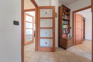 A hallway with a wooden door, a bookshelf, and a tiled floor. - The Terrace on the Gulf of Alghero 1 (Alghero)