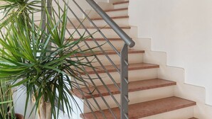 Eine Treppe mit Metallgeländer, beigen Stufen und Blumentöpfen am Fuß.