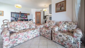 Ein Wohnzimmer mit floraler Couch, einem Bücherregal und einem Essbereich mit Stühlen.