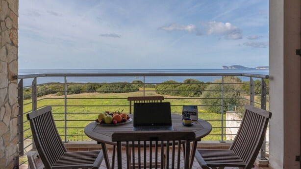 Ein Balkon mit Tisch, zwei Stühlen, einem Laptop und einer Obstplatte.
