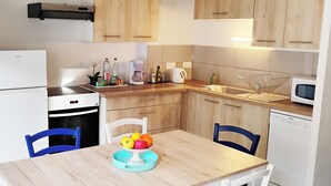 Una cocina moderna con armarios de madera, un refrigerador blanco, un lavavajillas y un microondas. Hay una mesa de comedor con sillas y un frutero sobre la mesa.