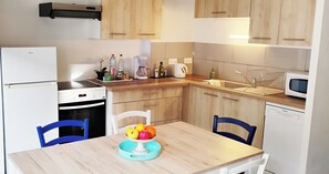 Eine moderne Küche mit Holzausziehtüren, einem weißen Kühlschrank, einem Geschirrspüler und einer Mikrowelle. Ein Esstisch mit Stühlen und eine Obstschale auf dem Tisch.