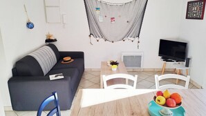 Una sala de estar con sofá, mesa de centro, televisor y un comedor con sillas y un frutero.