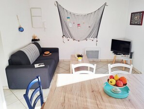 Ein Wohnzimmer mit einer Couch, einem Couchtisch, einem Fernseher und einem Essbereich mit Stühlen und einer Obstschale.