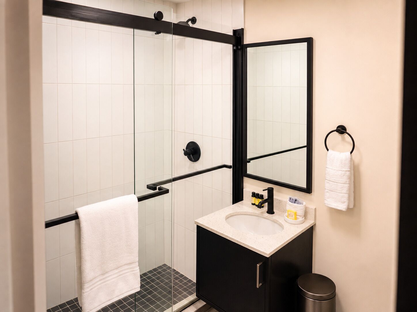 A modern bathroom with a glass shower enclosure, a black-framed mirror, a white sink, and a black cabinet.
