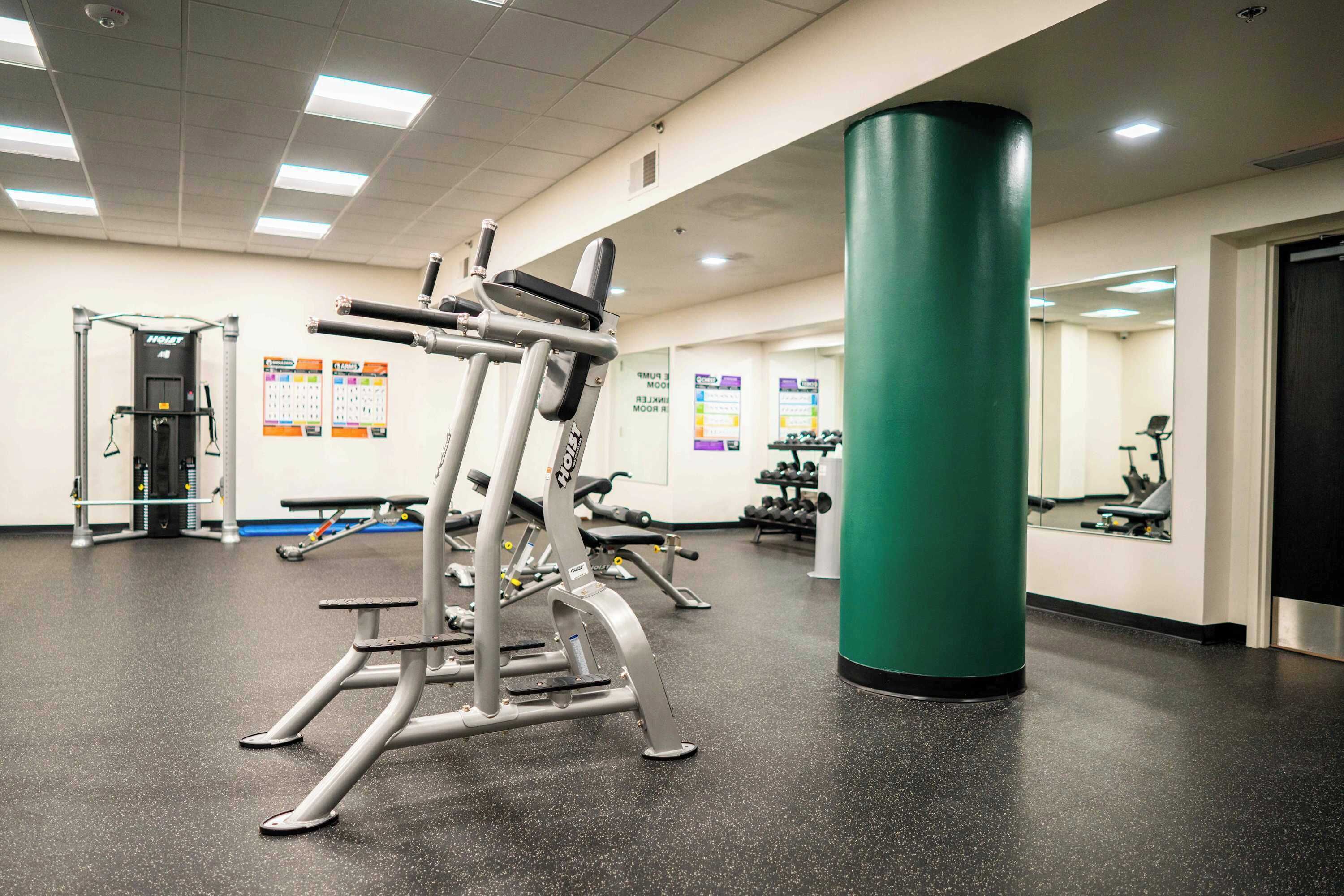 A gym with exercise equipment, a green pillar, and a mirrored wall.
