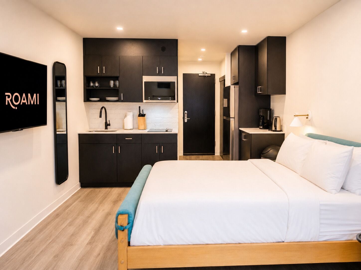 Quarto de hotel moderno com cama, televisão de tela plana, cozinha compacta e banheiro.