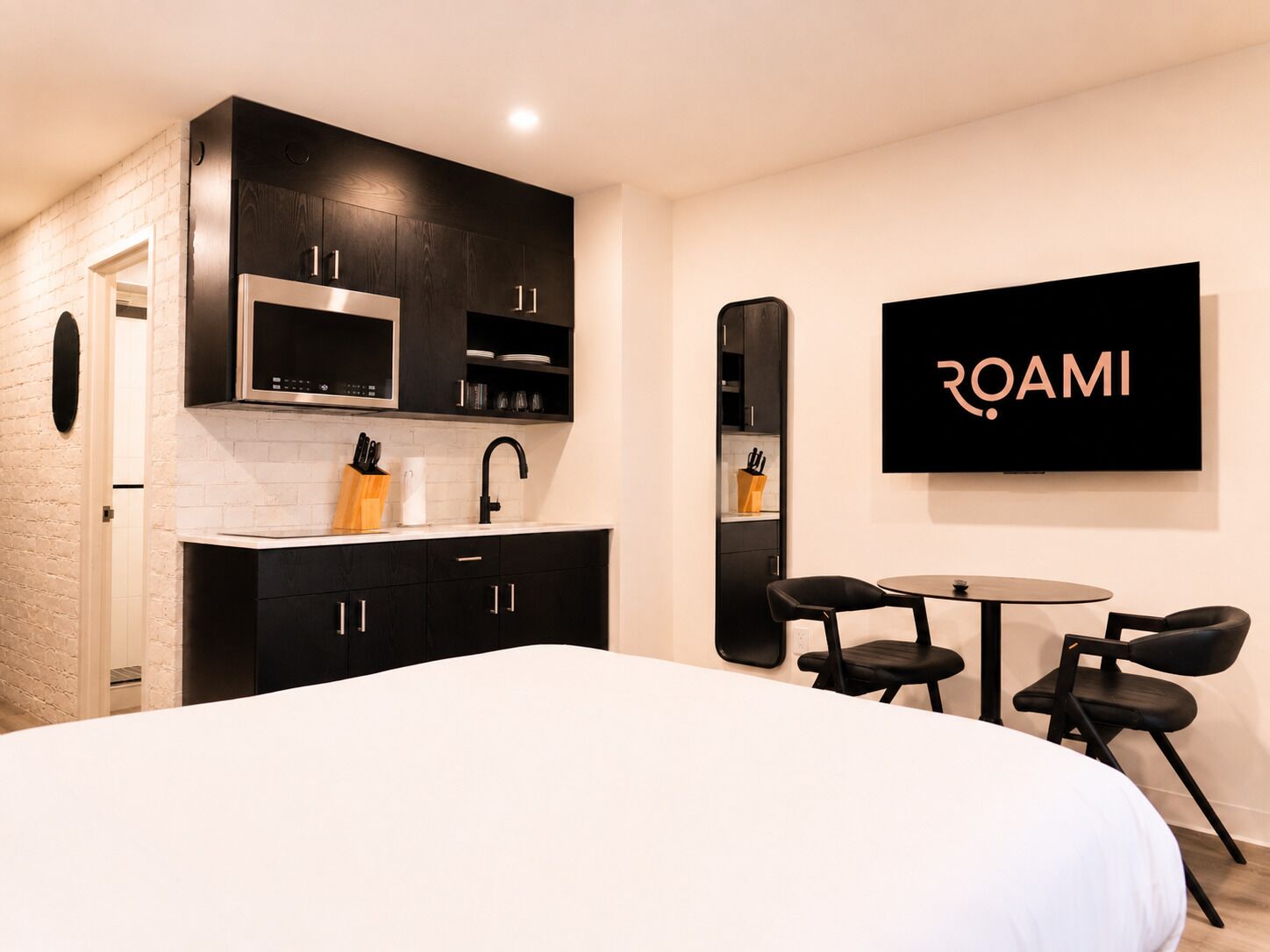 Una habitación de hotel moderna con kitchenette, una cama, un televisor y una zona de comedor.