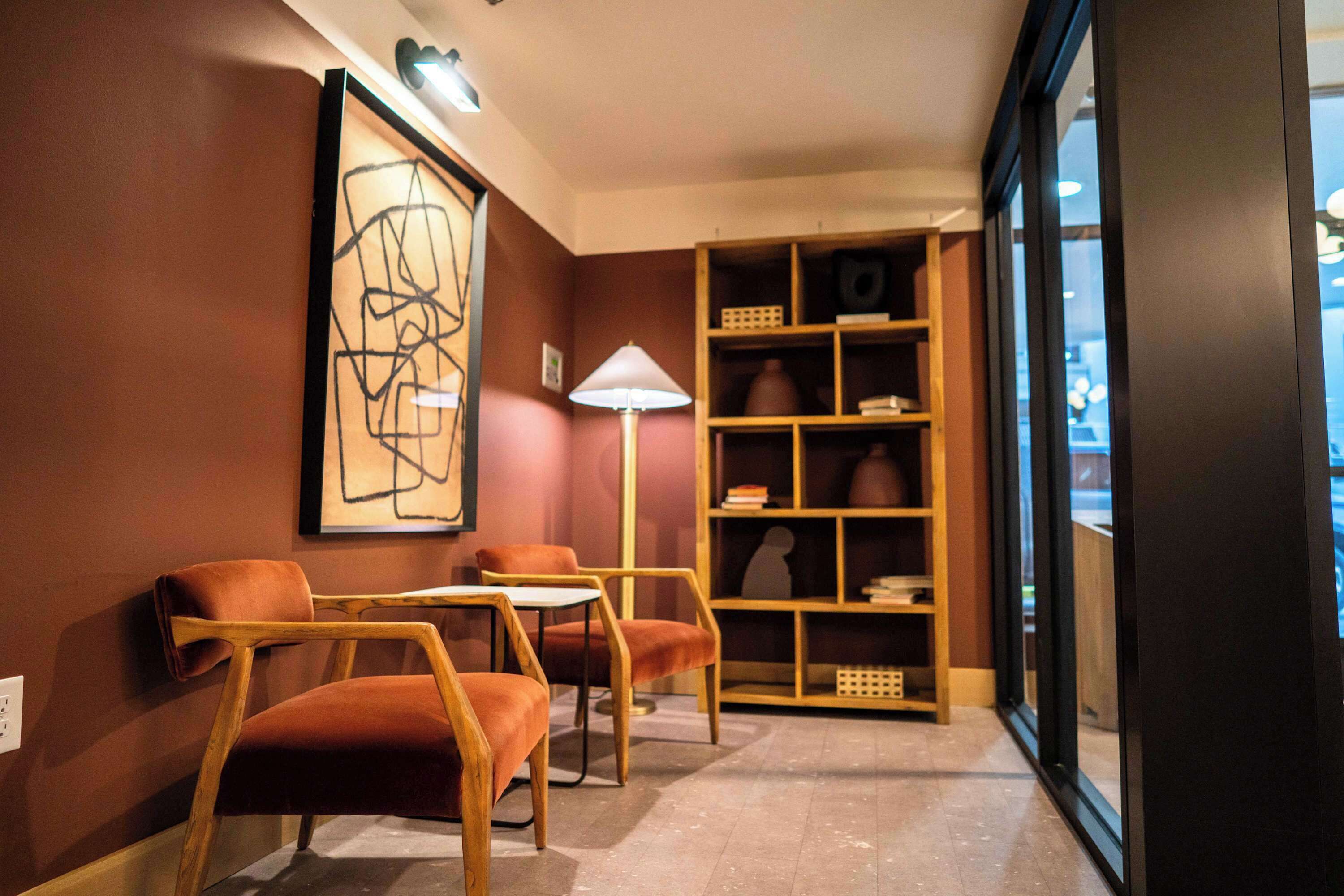 Un rincón acogedor con sillas de madera, una mesa, una estantería y una obra de arte abstracta enmarcada en la pared.