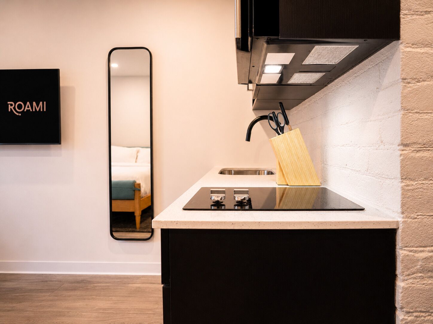 Een moderne keuken met een aanrecht, spoelbak en een spiegel die een bed weerspiegelt.