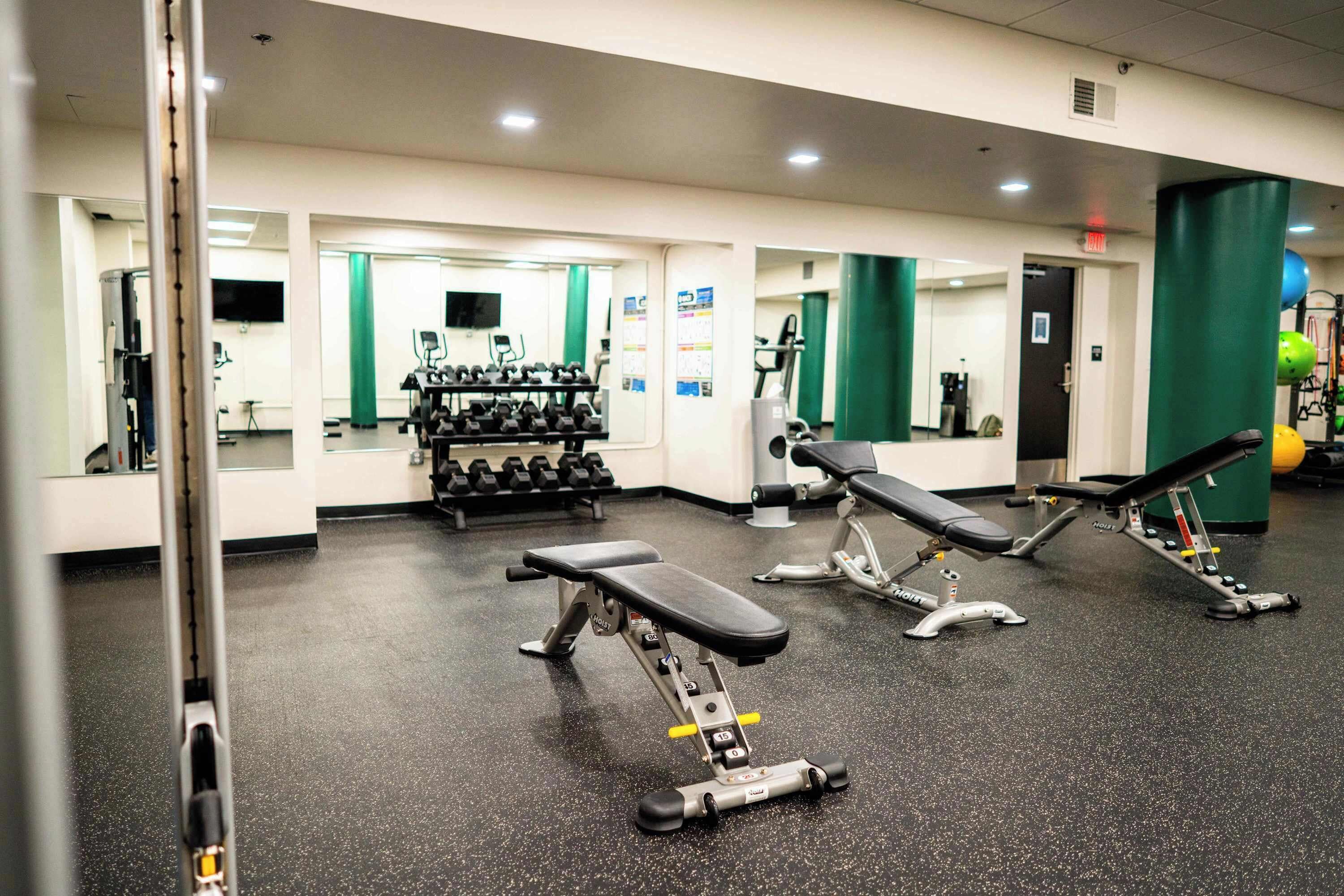 A gym with exercise equipment, a bench press, and a mirrored wall.