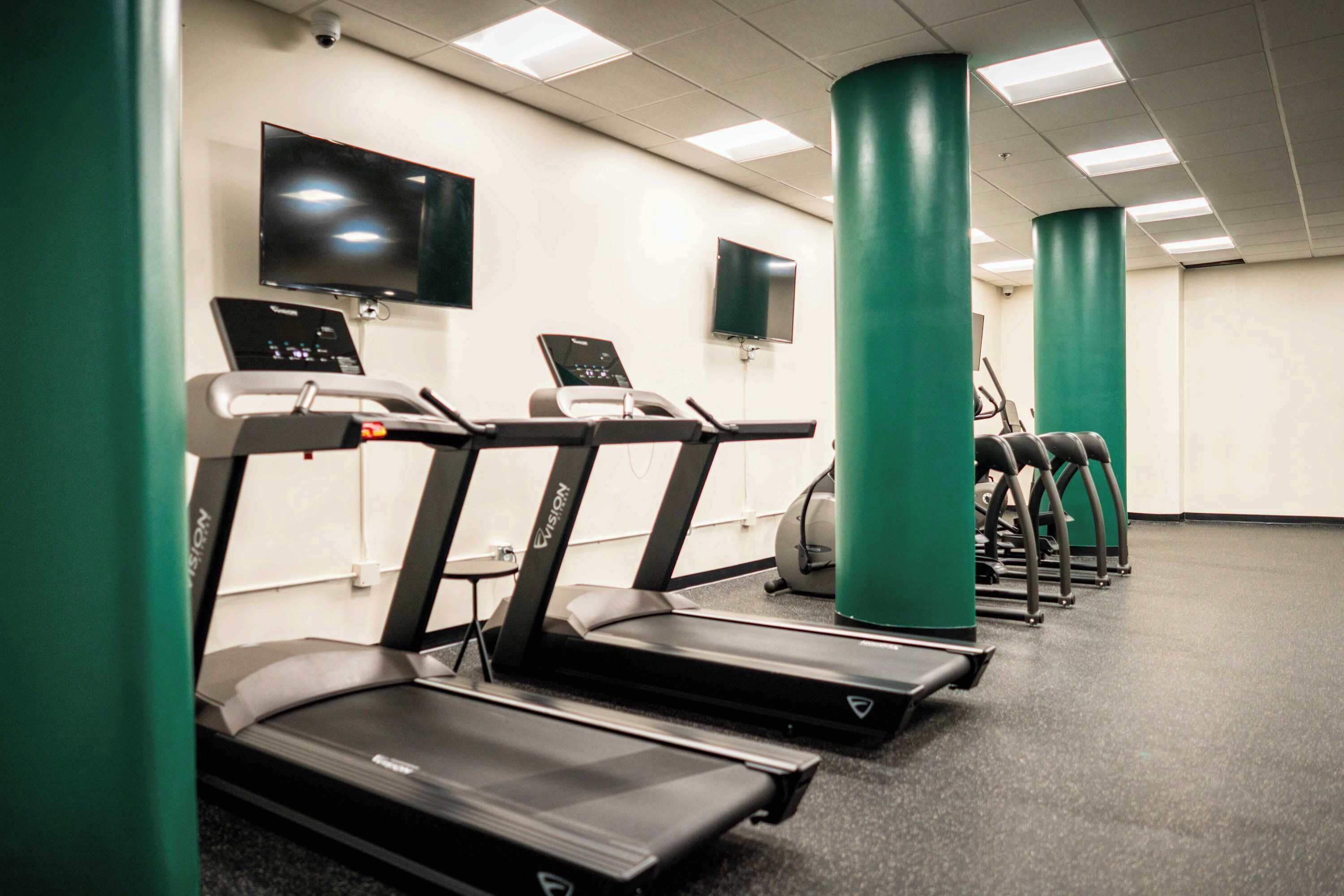 A gym with treadmills, exercise balls, and green pillars.