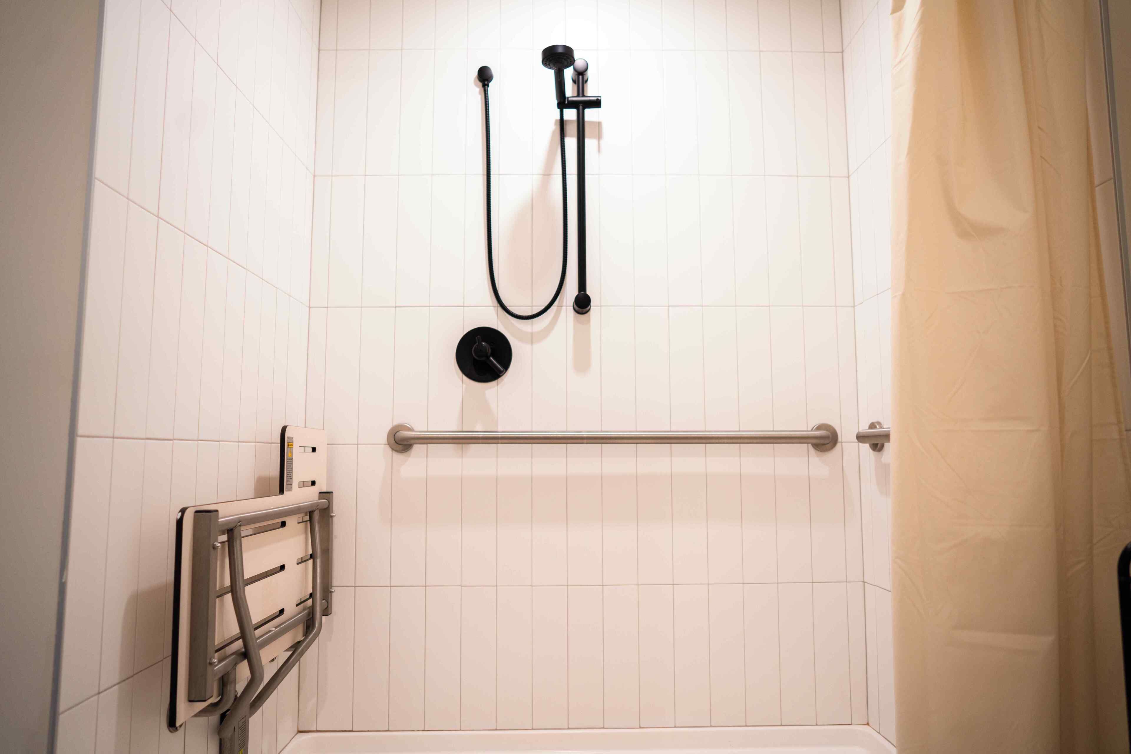 A shower with a handheld showerhead, a handheld faucet, and a grab bar.