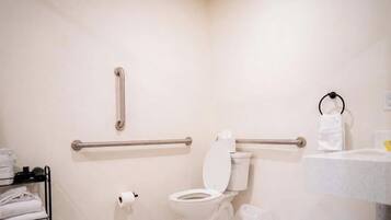 A bathroom with a toilet, handrails, a towel rack, and a sink.