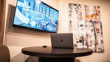 A modern room with a flat-screen TV displaying a room interior, a laptop on a table, and an abstract painting on the wall.